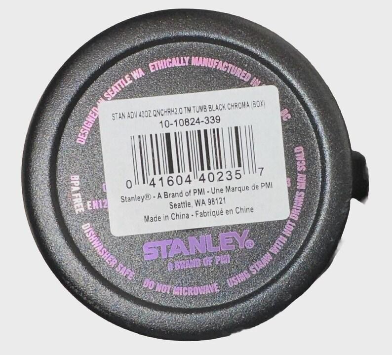 May include: A black Stanley tumbler bottom with a product label. The label includes the text "STAN ADV 40OZ QNCHRH2.0 TM TUMB BLACK CHROMA (BOX)" and a barcode. The tumbler is dishwasher safe and BPA free.