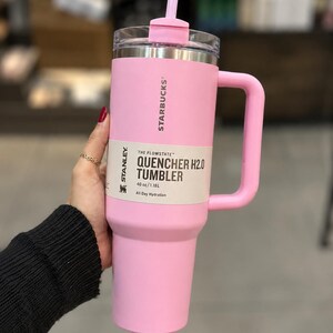 May include: A light pink Stanley Starbucks Quencher H2.0 tumbler with a 40 oz capacity. The cup features a matching pink handle, a clear lid with a pink straw, and a product label that reads The Flowstate Quencher H2.0 Tumbler 40 oz/1.18L.