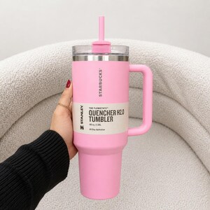 May include: A light pink Stanley Starbucks Quencher H2.0 tumbler with a matching straw, handle, and lid. The product label clearly displays the text: The Flowstate Quencher H2.0 Tumbler, 40 oz/1.18L, All Day Hydration, and the Stanley logo.