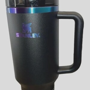 May include: Black Stanley Quencher H2.0 Tumbler with a handle and a straw. The tumbler has a black lid and a band of iridescent color around the top. The Stanley logo is visible on the side. The tumbler holds 40 oz (1.18L).