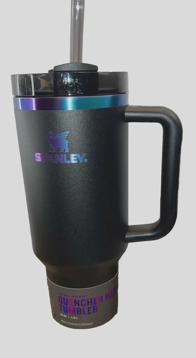May include: Black Stanley Quencher H2.0 Tumbler with a handle and a straw. The tumbler has a black lid and a band of iridescent color around the top. The Stanley logo is visible on the side. The tumbler holds 40 oz (1.18L).