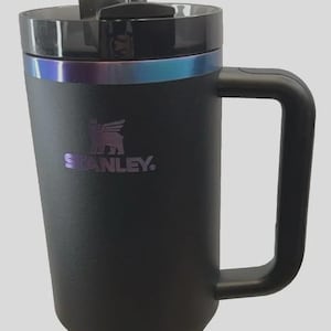 May include: Black Stanley Quencher Tumbler with a handle and straw. The tumbler has a black lid with a silver and blue iridescent band. The Stanley logo is visible on the front. The tumbler is part of the Black Chrome Collection.