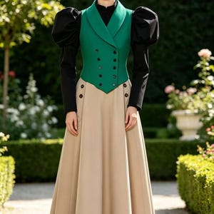 Op de afbeelding: Een formele outfit met een groen dubbelknoops vest met zwarte knopen, zwarte lange mouwen met pofmouwen en een beige rok. De outfit wordt gedragen door een persoon in een tuin.
