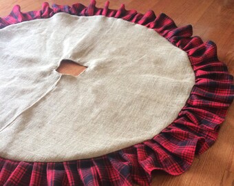 May include: A round burlap Christmas tree skirt with a red and black plaid ruffled edge. The skirt has a center opening for the tree trunk and is designed to sit on the floor.