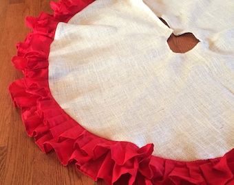 May include: A round, off-white burlap Christmas tree skirt with a vibrant red ruffled edge. The skirt has a circular opening in the center for the tree trunk. The red ruffle adds a decorative touch to the holiday decor.