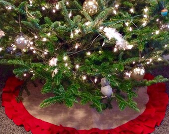 May include: A decorated Christmas tree with ornaments and lights. The tree sits on a burlap tree skirt with a red ruffled edge. The ornaments include glass balls, wooden cutouts, and small bird figurines.