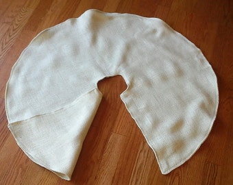 May include: A cream-colored, circular tree skirt made of a textured fabric. The skirt has a curved shape with a slit for the tree trunk. The fabric appears to be a natural fiber, possibly linen or burlap.