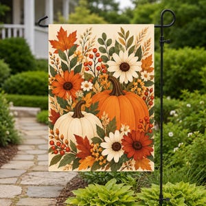 Op de afbeelding: Een rechthoekige tuin vlag met een herfstachtige illustratie van een grote oranje pompoen en een kleinere witte pompoen, omringd door witte en oranje madeliefjes, rode bessen en diverse esdoornbladeren in herfstkleuren.