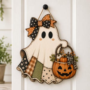 May include: A hanging wall decoration shaped like a ghost with a cream-colored body, black oval eyes, and pink cheeks. The ghost wears a patterned bow and carries a jack-o'-lantern basket filled with miniature pumpkins, berries, and green leaves.
