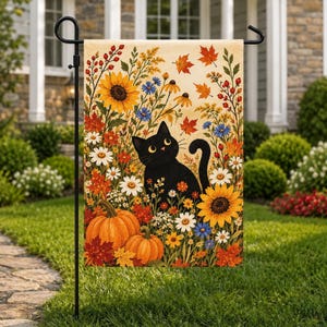 Puede incluir: Una bandera de jardín rectangular que presenta un gato negro sentado entre flores de otoño, incluyendo girasoles amarillos, margaritas blancas y flores silvestres azules, con dos calabazas naranjas y hojas de arce rojas sobre un fondo crema.