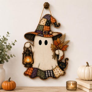 Peut inclure: Une décoration murale représentant un fantôme blanc portant un chapeau de sorcière en patchwork aux motifs orange, violets et verts. Le fantôme tient une lanterne allumée et un bouquet de feuilles d'automne, avec un petit chat noir en bas.