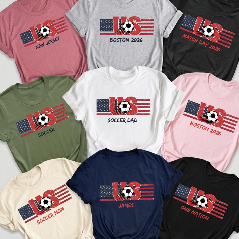 May include: A collection of nine short-sleeved t-shirts in various colors including pink, gray, black, olive green, white, and navy. Each shirt features a graphic of a soccer ball integrated into the letters US with a stylized American flag design.
