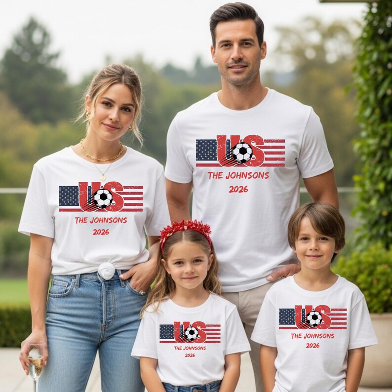 May include: A white short-sleeve t-shirt featuring a graphic of the American flag, a soccer ball, and the text US, THE JOHNSONS, and 2026. The design has a distressed, vintage-inspired texture with red, white, and blue colors throughout the print.