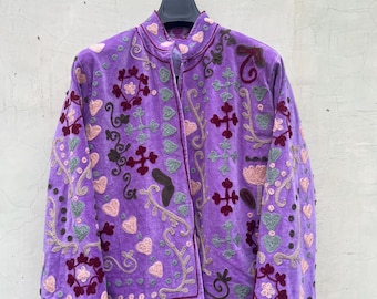 May include: A long-sleeved purple jacket featuring a mandarin collar and an open front. The garment is decorated with embroidered patterns in shades of dark red, light pink, and sage green, including heart shapes, floral motifs, and crosses.
