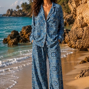 Op de afbeelding: Een tweedelige pyjamaset bestaande uit een overhemd met lange mouwen en knoopsluiting en een wijde broek met een blauw en wit bloemen-paisleypatroon. Het overhemd heeft een reverskraag, een borstzak en witte biezen langs de randen.