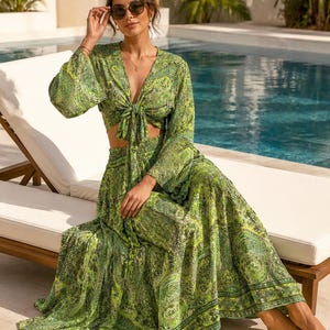 May include: A two-piece set consisting of a long-sleeved, V-neck crop top with a front tie closure and a matching high-waisted, floor-length maxi skirt. Both pieces feature an intricate, vibrant green paisley pattern with yellow and black details.