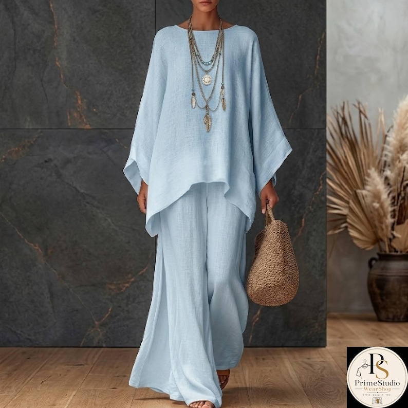 May include: A light blue linen two-piece outfit, consisting of a long-sleeved top and wide-leg pants. The top has a unique asymmetrical hemline. A woven straw handbag and layered necklaces complete the ensemble. The outfit is suitable for casual wear.