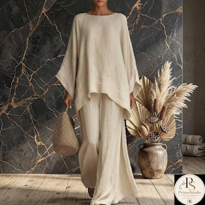 May include: A beige linen two-piece outfit, featuring a long-sleeved top with a wide neckline and matching wide-leg pants. The outfit is paired with a woven tote bag. The background has a dark marble effect.
