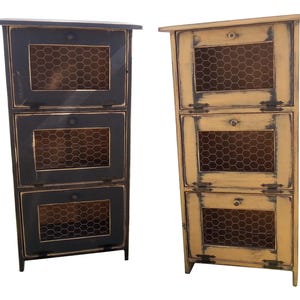 May include: Two rustic, three-drawer storage cabinets. One is black with a distressed finish, the other is a light yellow with a distressed finish. Each drawer has a wire mesh front and a small round knob.