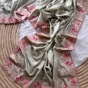 May include: A light sage green fabric drape featuring a scalloped border with intricate floral embroidery in shades of pink, magenta, and cream. The embroidery includes detailed rose motifs and small silver bead accents along the edges.