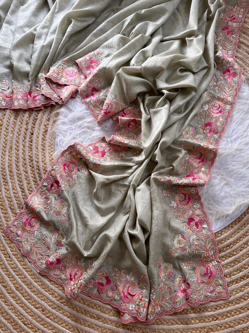 May include: A light sage green fabric drape featuring a scalloped border with intricate floral embroidery in shades of pink, magenta, and cream. The embroidery includes detailed rose motifs and small silver bead accents along the edges.