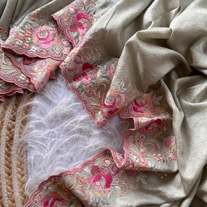 May include: A light beige fabric with a crinkled texture featuring a scalloped border. The border is decorated with intricate floral embroidery in shades of bright pink, soft peach, and sage green, accented with small clear sequins throughout.