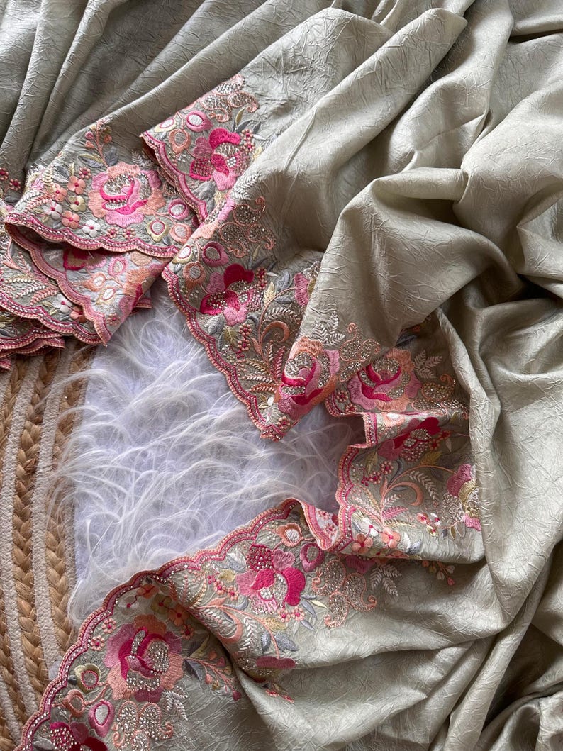 May include: A light beige fabric with a crinkled texture featuring a scalloped border. The border is decorated with intricate floral embroidery in shades of bright pink, soft peach, and sage green, accented with small clear sequins throughout.