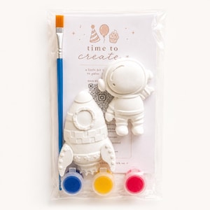 May include: A craft kit containing a rocket ship and astronaut figurine, a blue-handled paintbrush, and three paint pots. The packaging displays the text "time to create".