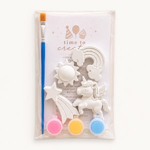 May include: A craft kit featuring a blue-handled paintbrush, a white unicorn, rainbow, sun, star, and three paint pots in pink, yellow, and blue. The kit is packaged in a clear plastic bag with the words "time to create".