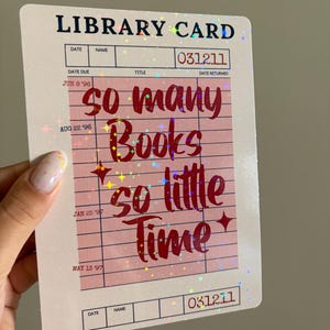 Puede incluir: Un diseño de tarjeta de biblioteca con el texto "so many books so little time" en fuente cursiva. La tarjeta tiene un fondo rosa con un patrón de cuadrícula y acentos holográficos. La tarjeta también incluye el texto "LIBRARY CARD" y los números "031211".