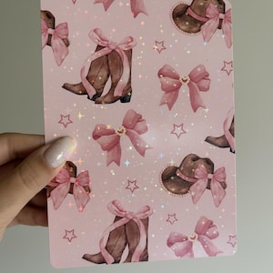 Peut inclure: Une carte rose avec un motif répété de bottes de cowboy marron, de nœuds et de chapeaux, tous ornés de nœuds roses. Le motif comprend des étoiles et un léger effet scintillant.