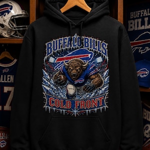 Op de afbeelding: Een zwarte hoodie met een afbeelding van een buffelspeler in een blauw shirt die een football vasthoudt. De tekst luidt Buffalo Bills en Cold Front. Het ontwerp bevat ijzige accenten, stadionverlichting en het teamlogo in blauw, rood en wit.