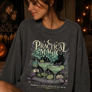 以下が含まれることがあります： Practical Magic、Midnight Margaritas、There's a little witch in all of usというテキストがプリントされた、ペッパーカラーのクルーネックスウェットシャツ。デザインには、ブレンダー、2つのマルガリータ、黒猫、花が描かれています。