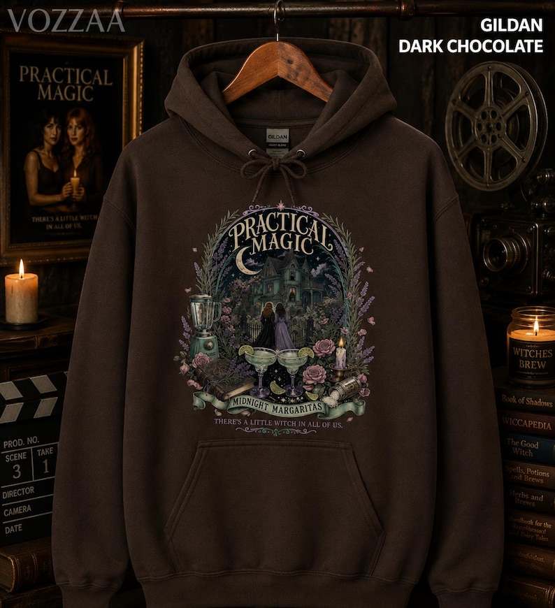 Op de afbeelding: Een donker chocoladebruine hoodie met een grafische print met de tekst Practical Magic, Midnight Margaritas en There's a little witch in all of us. Het ontwerp bevat een huis, twee figuren, margarita's en diverse florale elementen.