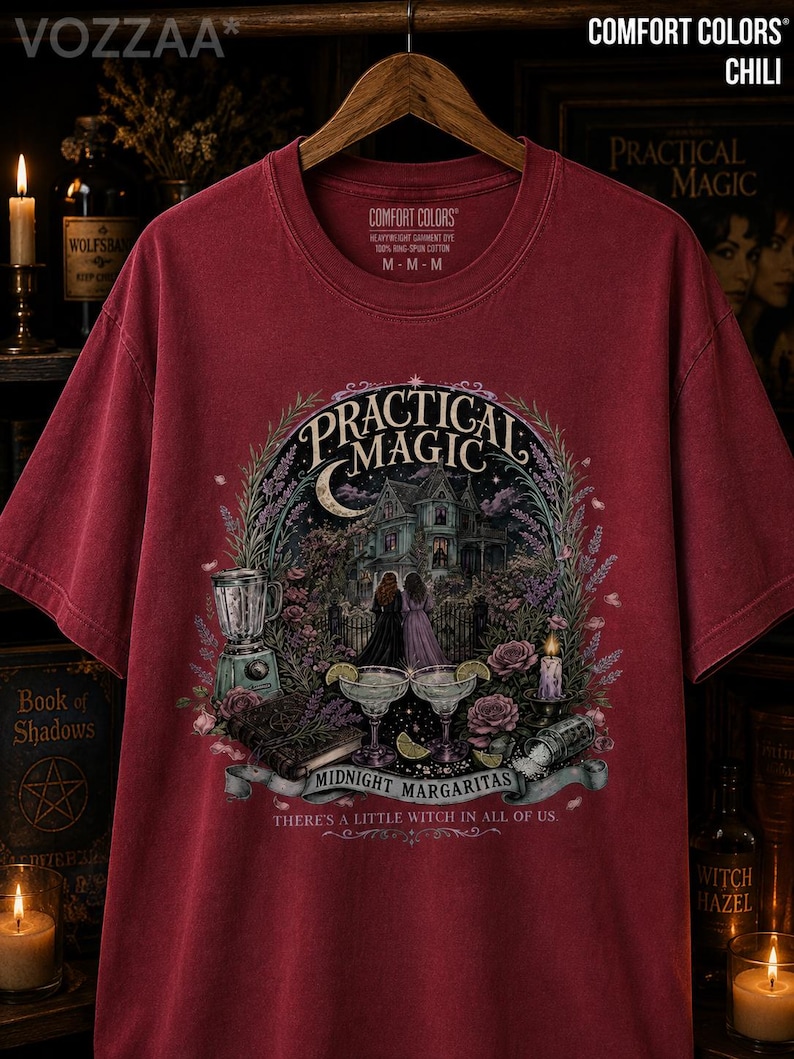 May include: A chili red short-sleeve t-shirt featuring a graphic print of a house, two figures, margaritas, and a blender. The text reads Practical Magic, Midnight Margaritas, and There's a Little Witch in All of Us. The shirt has a crew neckline.