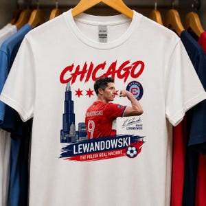 May include: A white t-shirt featuring a graphic of Robert Lewandowski in a red soccer jersey flexing his arm. The design includes the Chicago skyline, the text CHICAGO, LEWANDOWSKI, THE POLISH GOAL MACHINE, a soccer ball, and a signature.