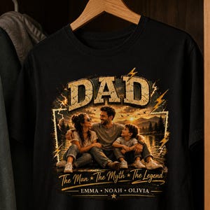 May include: Black t-shirt with a graphic featuring the word "DAD" in a distressed gold font. The graphic includes a family portrait with the text "The Man * The Myth * The Legend" and the names Emma, Noah, and Olivia.