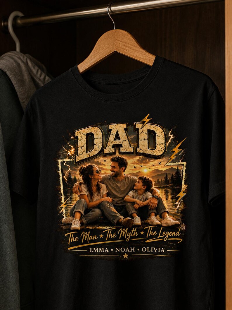 May include: Black t-shirt with a graphic featuring the word "DAD" in a distressed gold font. The graphic includes a family portrait with the text "The Man * The Myth * The Legend" and the names Emma, Noah, and Olivia.