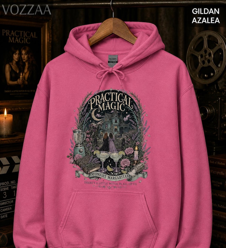 Op de afbeelding: Een felroze hoodie met een grafische print op de voorzijde. Het ontwerp toont een huis, twee figuren, een blender, twee margaritaglazen en een boek, met de tekst "PRACTICAL MAGIC MIDNIGHT MARGARITAS THERE'S A LITTLE WITCH IN ALL OF US."