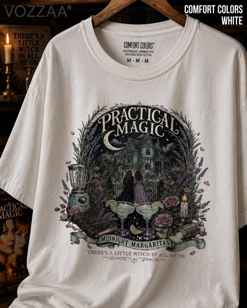 May include: A white t-shirt featuring a graphic print with the text "PRACTICAL MAGIC", "MIDNIGHT MARGARITAS", and "THERE'S A LITTLE WITCH IN ALL OF US." The design includes a house, two figures, a blender, two margaritas, a book, and flowers.