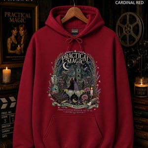 Op de afbeelding: Een kardinaalrode hoodie met een grafische print met de tekst Practical Magic, Midnight Margaritas en There's a little witch in all of us. Het ontwerp bevat een huis, twee figuren, een blender en twee margaritaglazen.