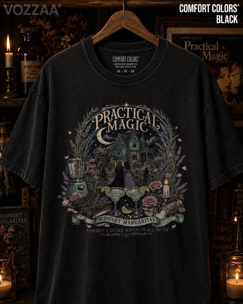 May include: A black short-sleeve t-shirt featuring a graphic print with the text "PRACTICAL MAGIC", "MIDNIGHT MARGARITAS", and "THERE'S A LITTLE WITCH IN ALL OF US". The design includes a house, two people, margaritas, a blender, and flowers.