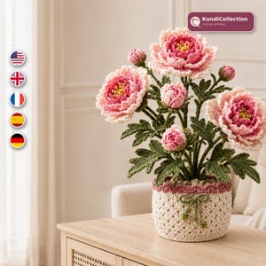 May include: A crochet flower arrangement featuring three large, multi-layered pink and white peony blossoms and three smaller buds. The flowers have dark green crocheted leaves and stems, all housed in a cream-colored crocheted pot with a small bow.