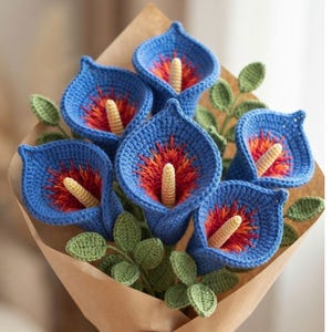 May include: A bouquet of six crocheted calla lily flowers featuring vibrant blue petals with a textured orange and red center and a pale yellow spadix. The flowers are accompanied by small green crocheted leaves and wrapped in brown paper.