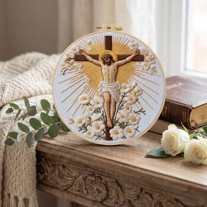 May include: A circular embroidery hoop featuring a detailed needlework depiction of a figure on a cross, surrounded by embroidered white flowers and golden sunburst rays on a white fabric background, framed in a light-colored wooden hoop.