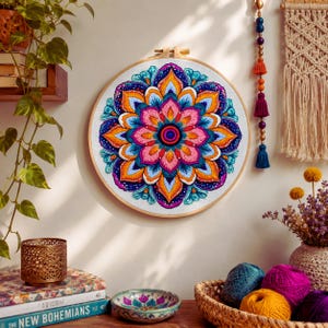 May include: A circular embroidery hoop featuring a vibrant, multi-colored mandala design with intricate stitching in shades of pink, orange, yellow, and teal on a white fabric background, displayed as a piece of wall art with a wooden frame.