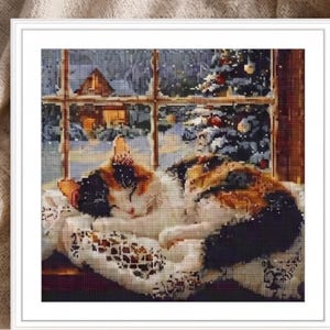 May include: A square diamond painting kit featuring a calico cat curled up on a white lace cloth. The cat is positioned in front of a window looking out at a snowy winter scene with a lit house and a decorated Christmas tree in the background.