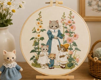 Puede incluir: Un bastidor de bordado circular de madera que contiene un panel de tela con una ilustración detallada de una familia de gatos entre flores de malva real. Los gatos visten ropa de estilo vintage, incluyendo vestidos y petos.