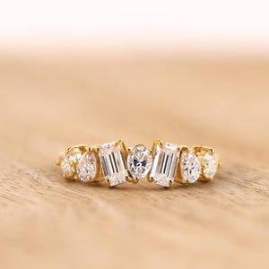 May include: A gold band ring featuring a multi-stone arrangement with two baguette-cut diamonds, two pear-cut diamonds, and three round brilliant-cut diamonds set in a horizontal row. The ring has a polished yellow gold finish and clear stones.