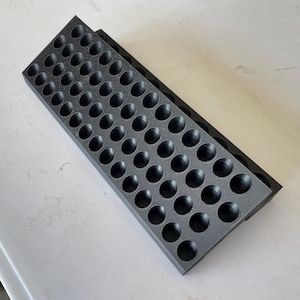May include: A rectangular black storage tray featuring a grid of fifty circular indentations arranged in five rows of ten. The tray has a textured surface finish and is constructed with a rigid, flat base and uniform, evenly spaced circular wells.